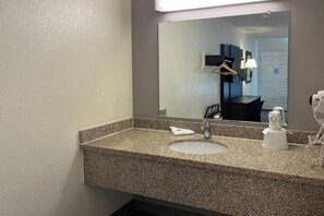 A bathroom with a granite countertop, a sink, a mirror, and a hairdryer.