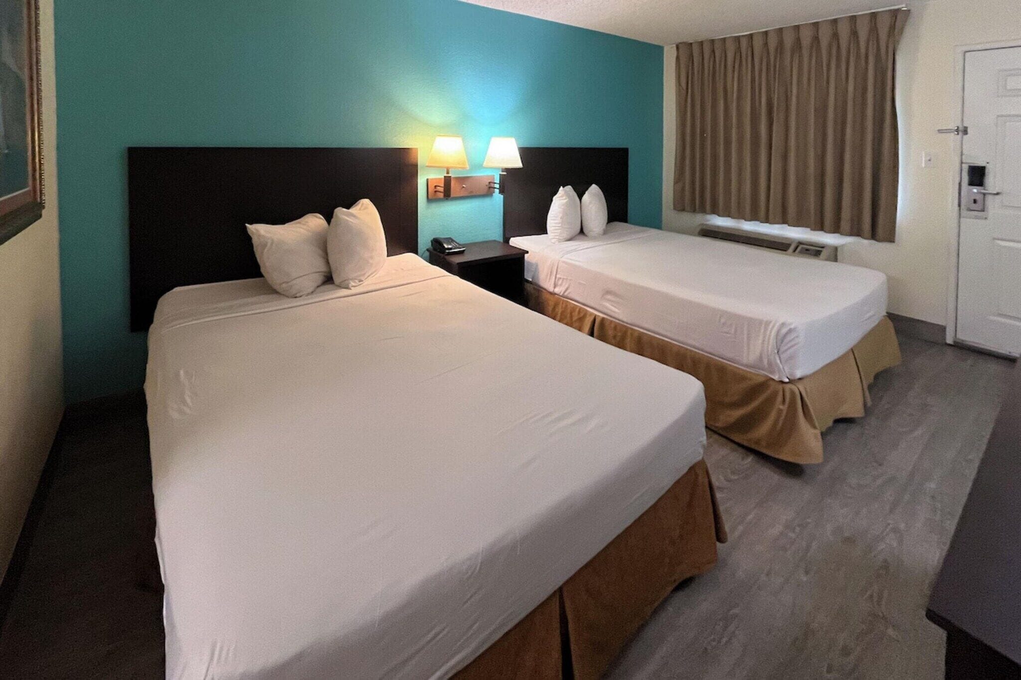 A hotel room with two beds, a nightstand, a lamp, a telephone, and a door.