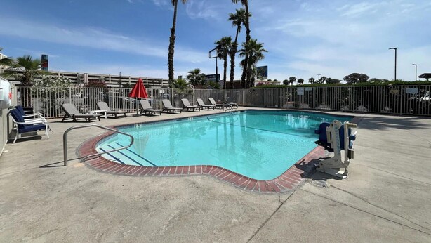 A swimming pool with a brick border, surrounded by lounge chairs and a red umbrella. - 1 Full Bed | Mobility Access RI Shwr, Nsmk (Las Vegas)