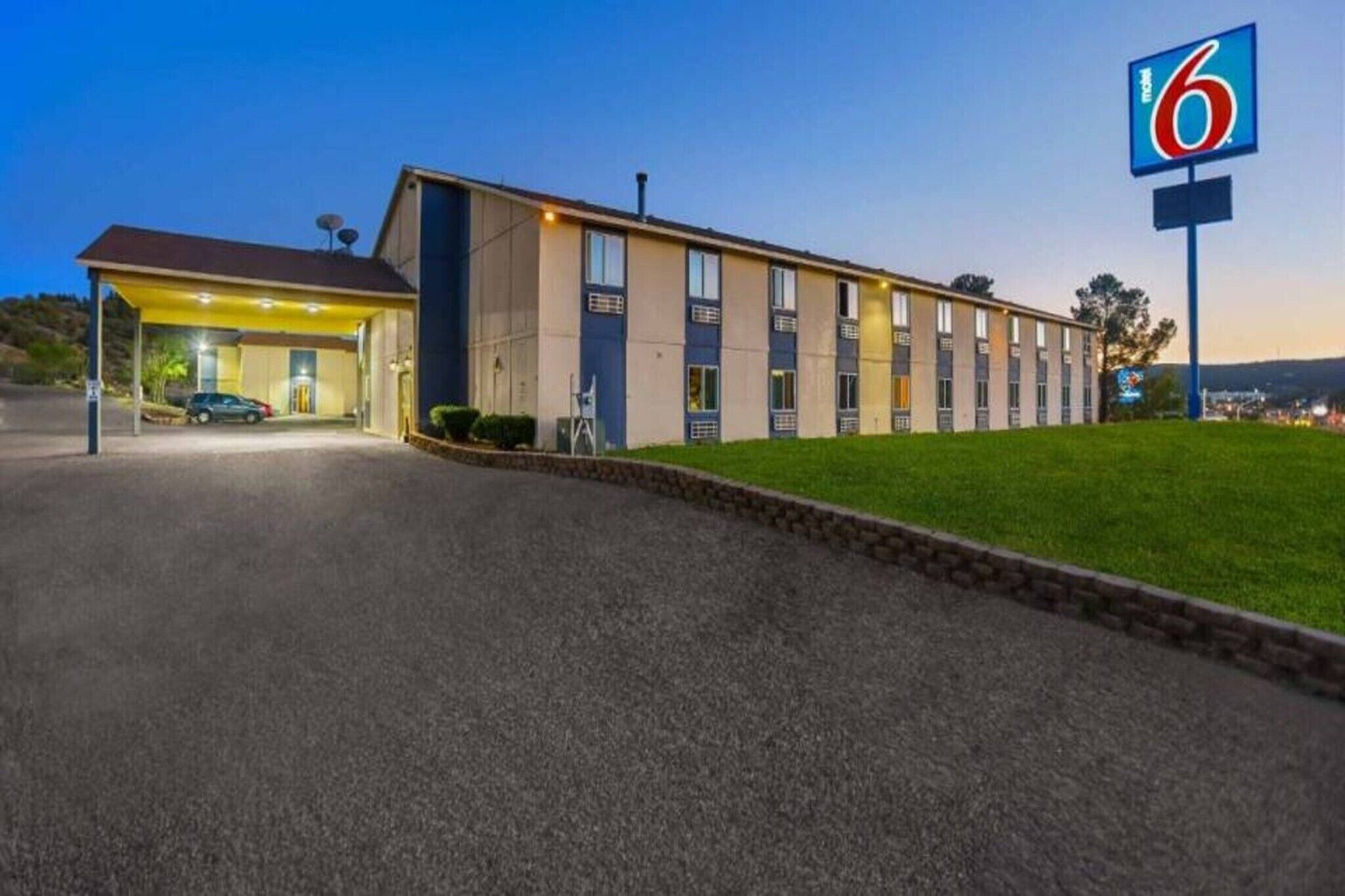 A motel with a single-story building, a covered parking area, and a well-maintained lawn.