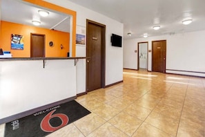 Un espace d’accueil d’hôtel comprenant un comptoir de réception, une horloge et un tapis d’entrée avec l’inscription « Bienvenue ».