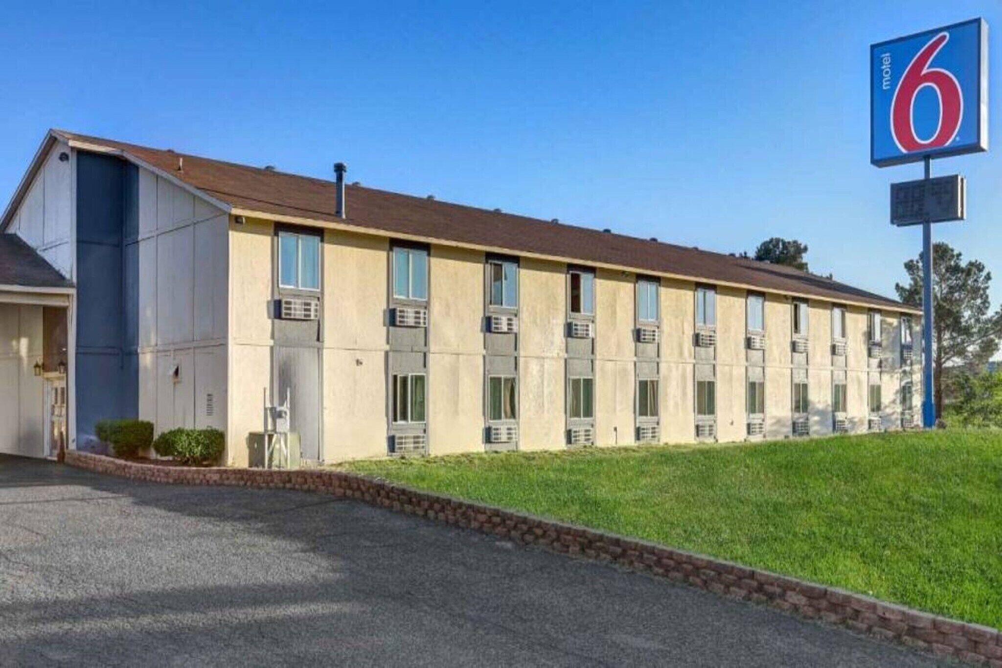 A motel with a row of rooms, a parking lot, and a grassy area.