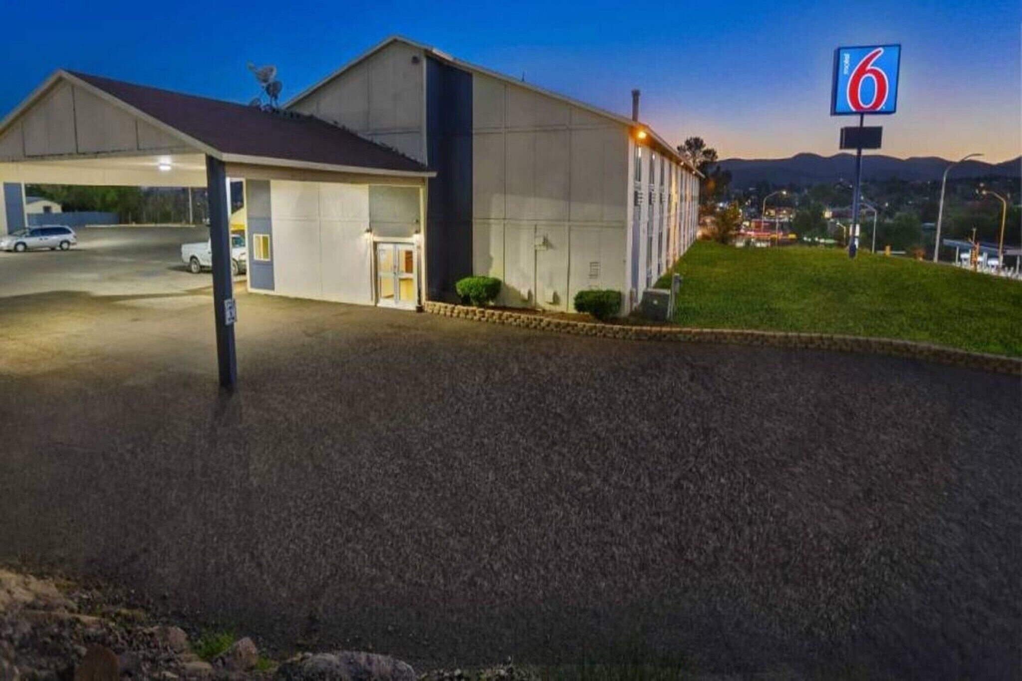 A motel with a covered parking area, a building with a flat roof, and a sign indicating the number 6.