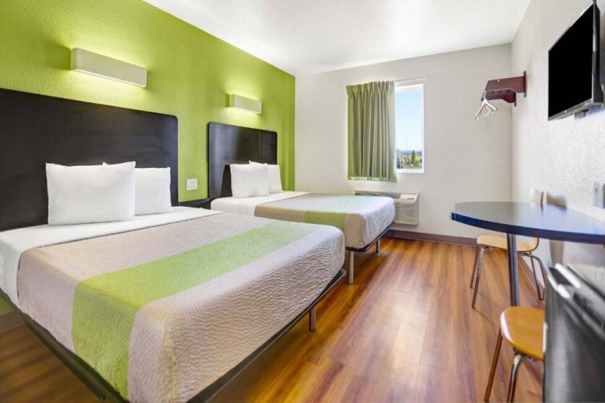 A hotel room with two beds, a desk, and a television.