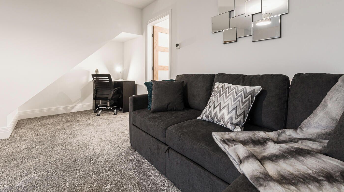 A modern living room with a dark grey sofa, a patterned throw blanket, and a desk with a chair.