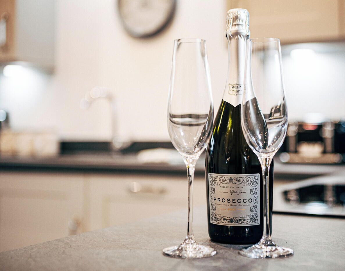 A bottle of Prosecco wine and two empty wine glasses on a table.
