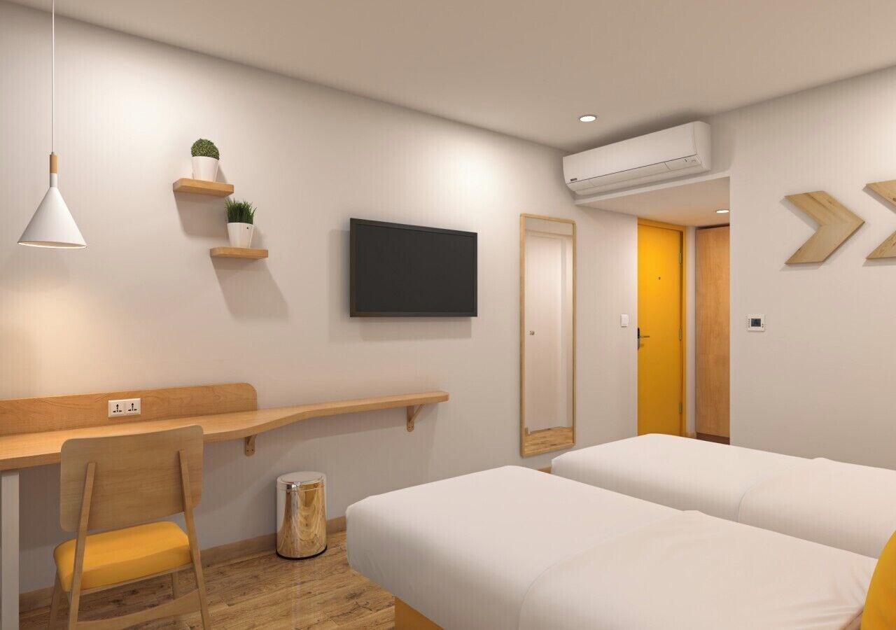Et moderne hotelværelse med skrivebord, to senge, et fjernsyn og en lille plante.