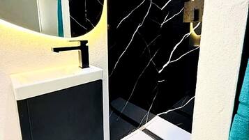 Un baño con diseño moderno, que presenta un lavamanos blanco, un mueble negro y una pared con estampado de mármol.