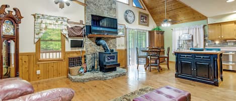 A spacious living area with a stone fireplace, wooden ceiling, and a television mounted above it.