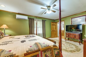 Ein Schlafzimmer mit einem Himmelbett, Deckenventilator, Klimaanlage, Fernseher auf einem Holzkasten und einer Tür zu einem weiteren Raum.