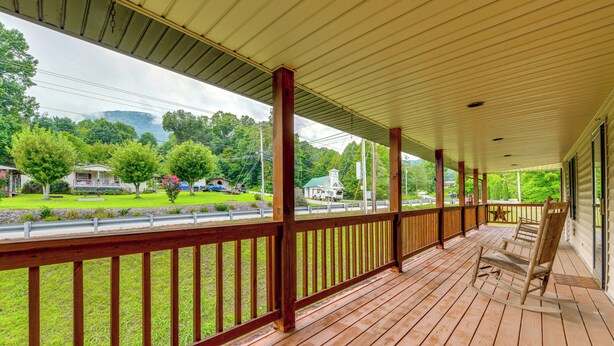 Una terrazza in legno coperta con ringhiera, affacciata su un paesaggio verde con alberi e una strada.