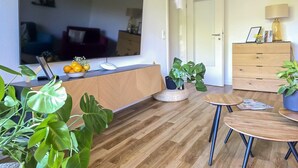 Ein Wohnzimmer mit Holzboden, einem Fernseher, einem Holzkasten, einem Esstisch und Topfpflanzen.