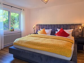 Una cama con cabecera, una mesita de noche y una ventana con cortinas.