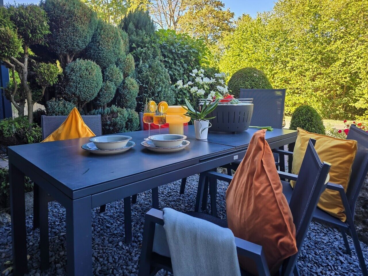 An outdoor dining area with a table set for two, surrounded by chairs and cushions.