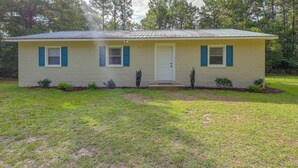 A single-story house with a front door, two windows with shutters, and a small porch area. - Quiet Country Living Near Whiteville (Whiteville)