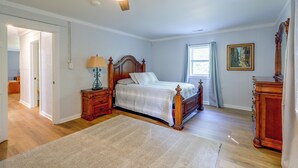A bedroom with a wooden bed, a nightstand, a lamp, a ceiling fan, a window with curtains, and a painting on the wall. - Quiet Country Living Near Whiteville (Whiteville)