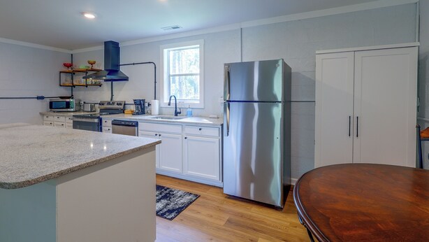 A modern kitchen with stainless steel appliances, white cabinetry, and a wooden dining table. - Quiet Country Living Near Whiteville (Whiteville)