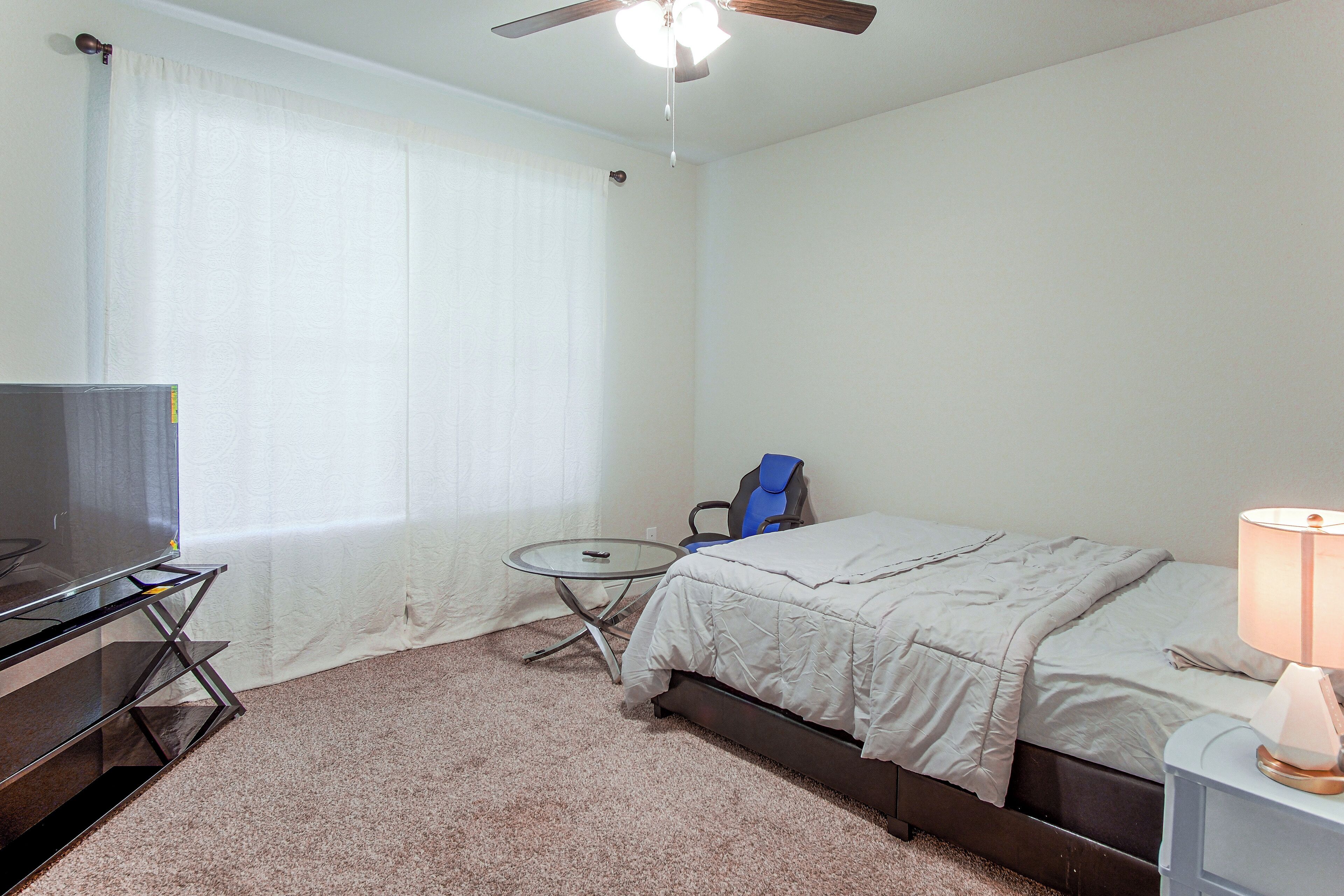 A hotel room with a bed, a desk with a television, a chair, a lamp, and a ceiling fan.