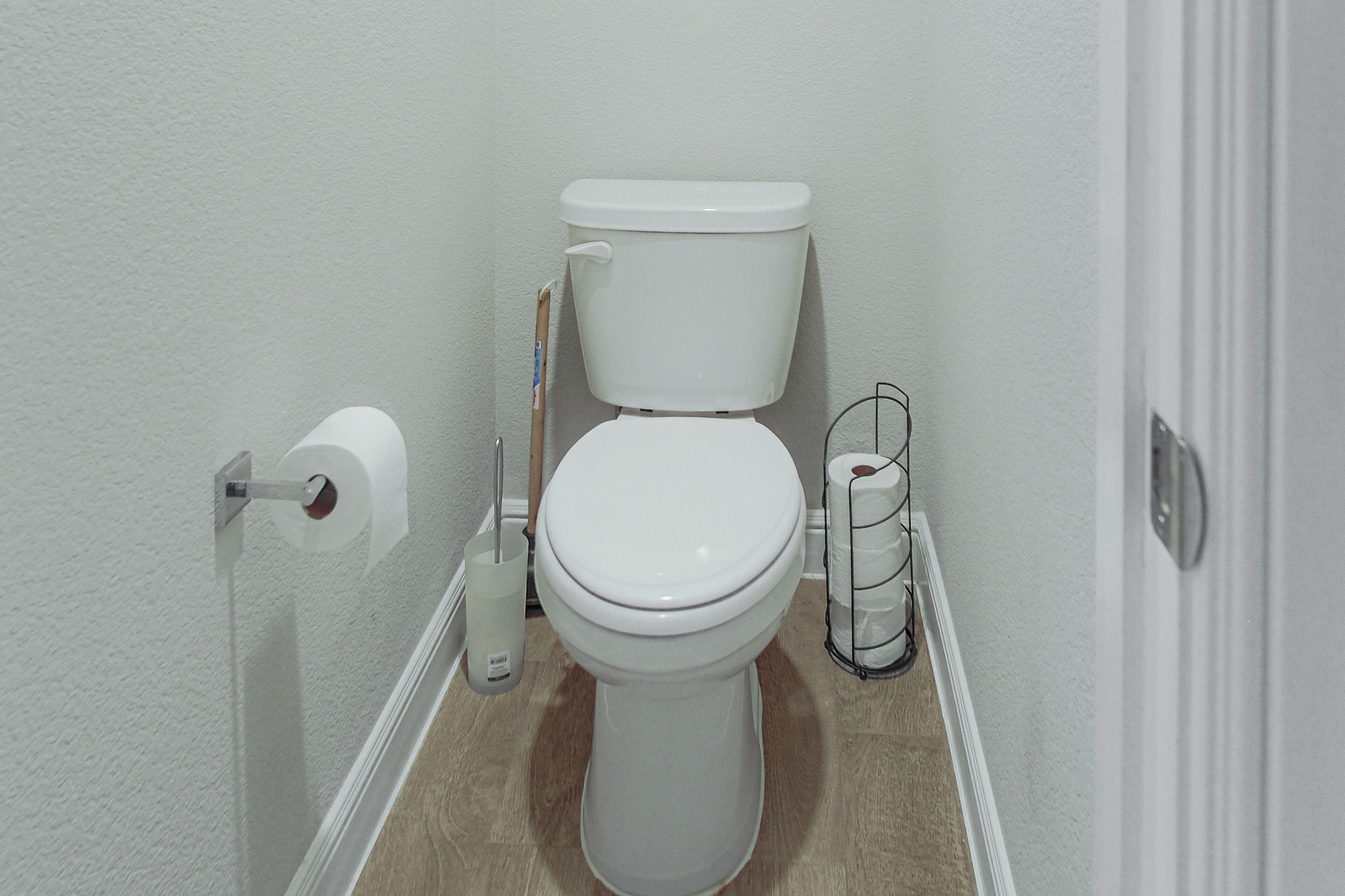 Een standaard wit toilet met een toiletpapierhouder en een spuitdouche aan de rechterkant.