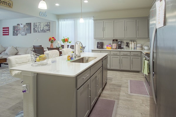 Una cocina moderna con una isla central, electrodomésticos de acero inoxidable y una zona de comedor con sofá y sillas.