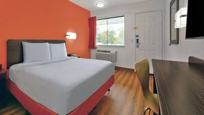 Ein Hotelzimmer mit Bett, Schreibtisch, Stuhl, Fenster und Klimaanlage.