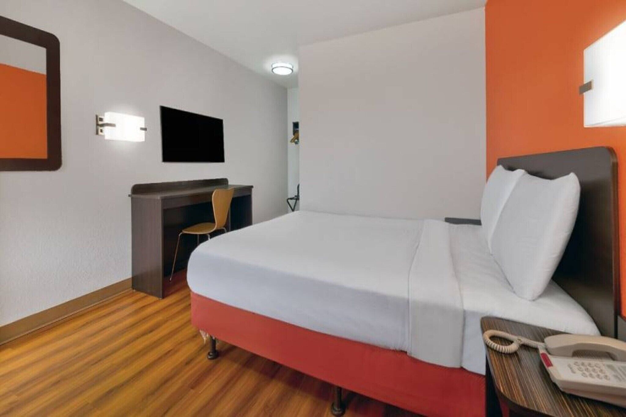 Ein Hotelzimmer mit Bett, Schreibtisch, Stuhl, Telefon und Fernseher.