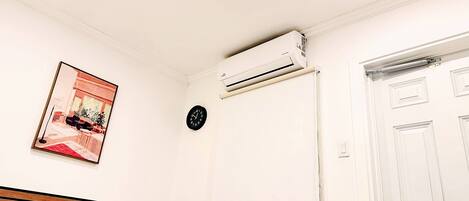 A bedroom with a bed, an air conditioning unit, a clock, and a door.