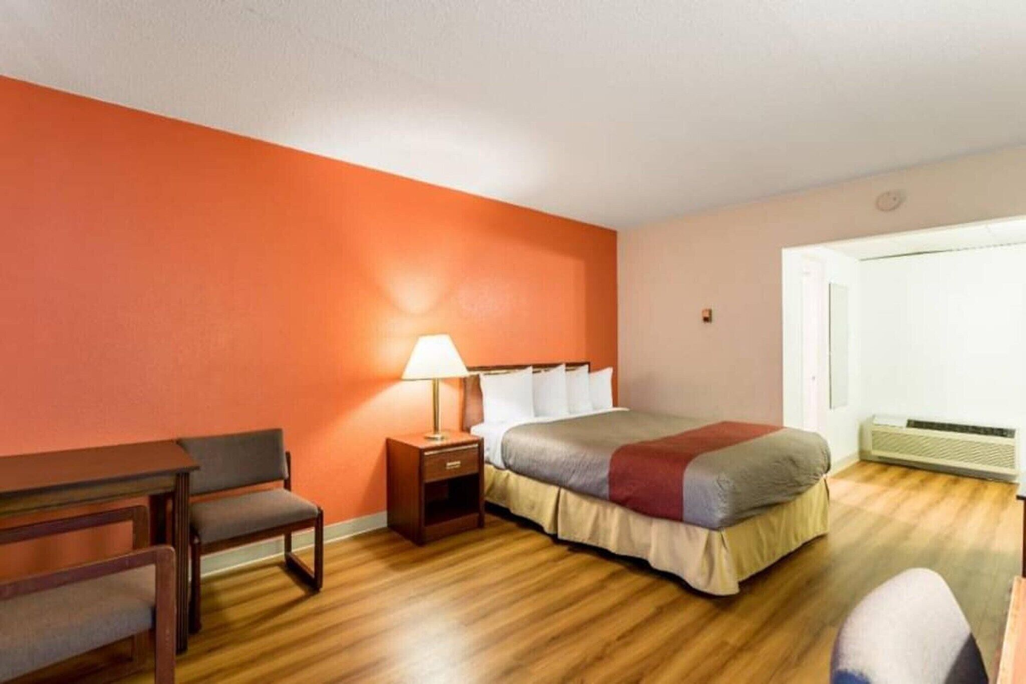 A hotel room with a bed, bedside table, lamp, chair, and a window with a view.