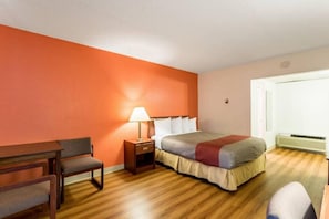 Una camera d'hotel con un letto, comodino, lampada, sedia e finestra con vista.