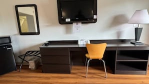 Ett kompakt hotellrum med ett skrivbord, en stol, en tv, en lampa och en papperskorg.