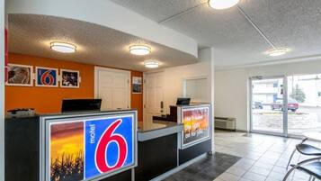 A motel lobby with a reception desk, a large number '6' sign, and a view of the parking area.
