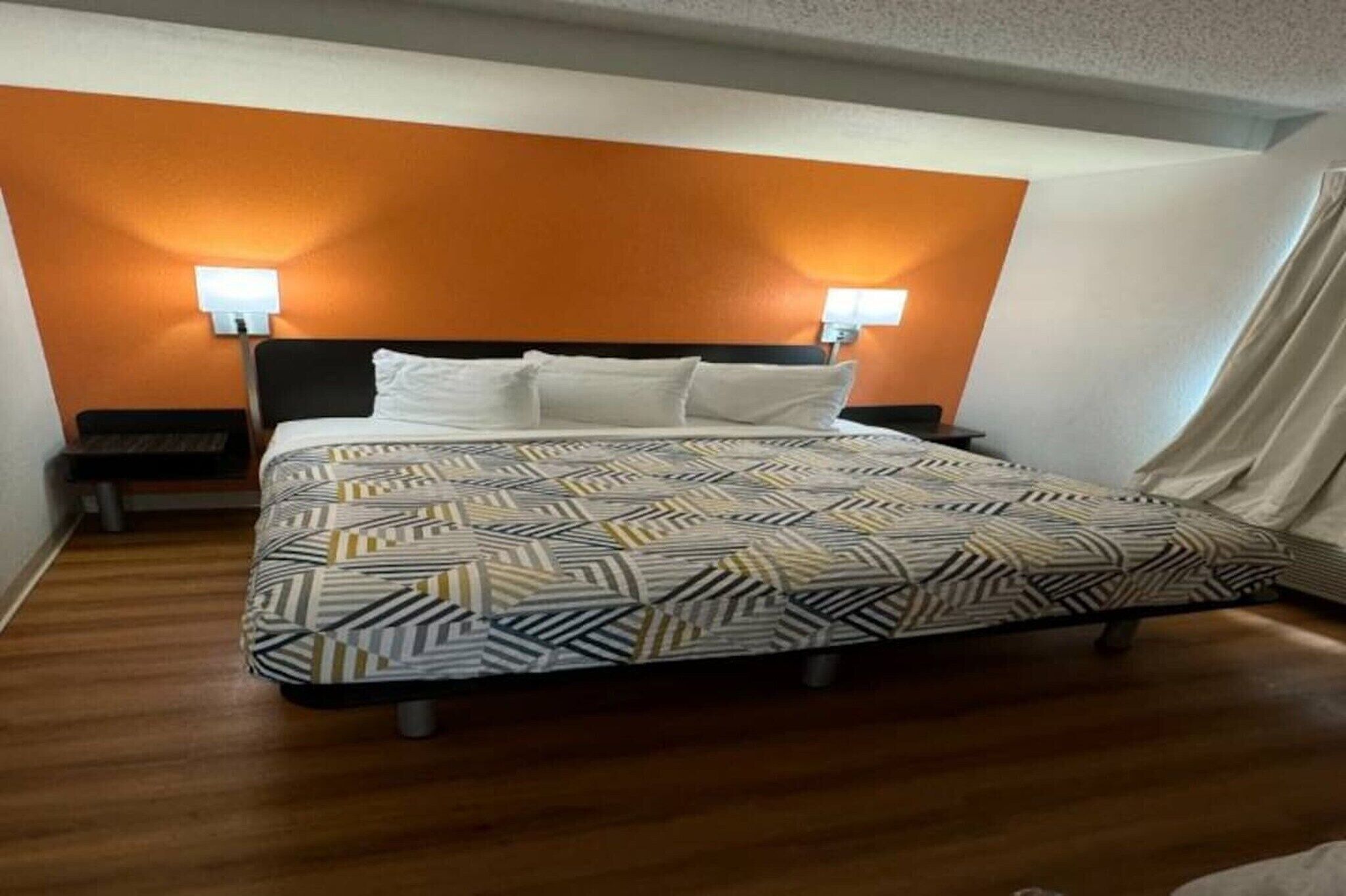 A hotel room with a bed, two bedside lamps, a nightstand, and a window with curtains.