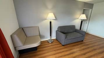 Ein Zimmer mit Holzboden, einem beigefarbenen Sofa, einem grauen Sessel und zwei Stehlampen.