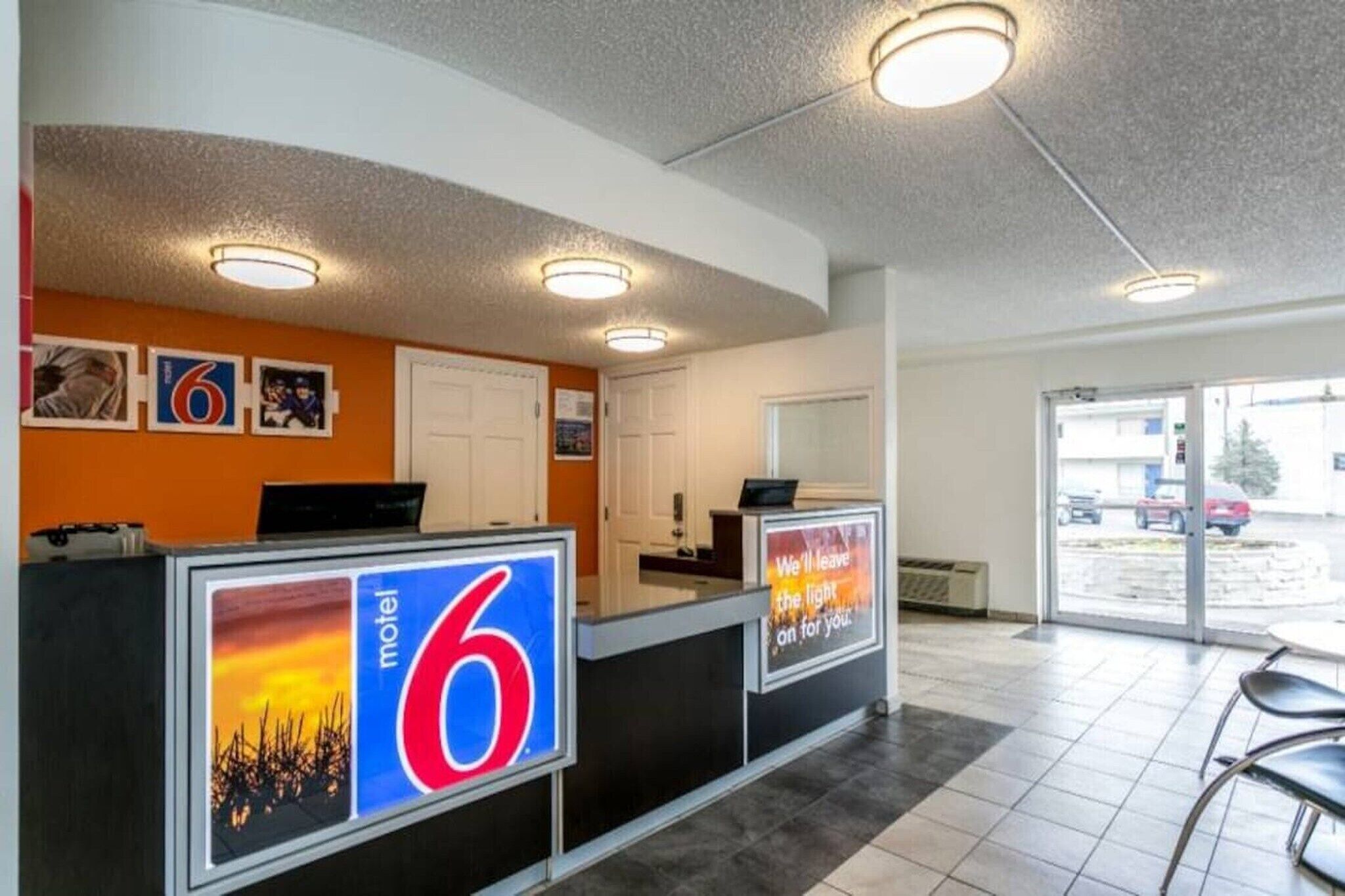 A motel lobby with a reception desk, a large number '6' sign, and a view of the parking area.