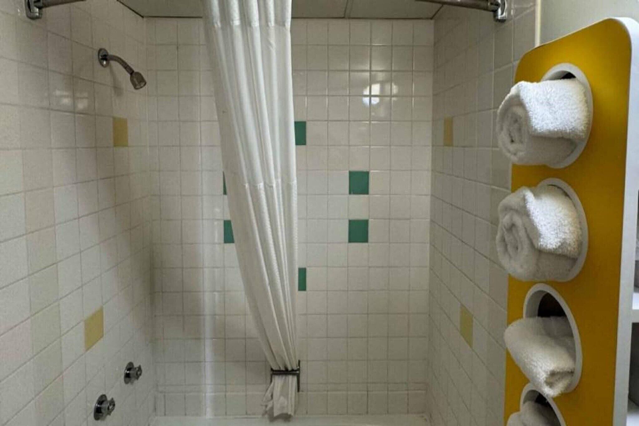 A shower stall with a white curtain, a yellow towel rack, and a tiled wall with green accents.