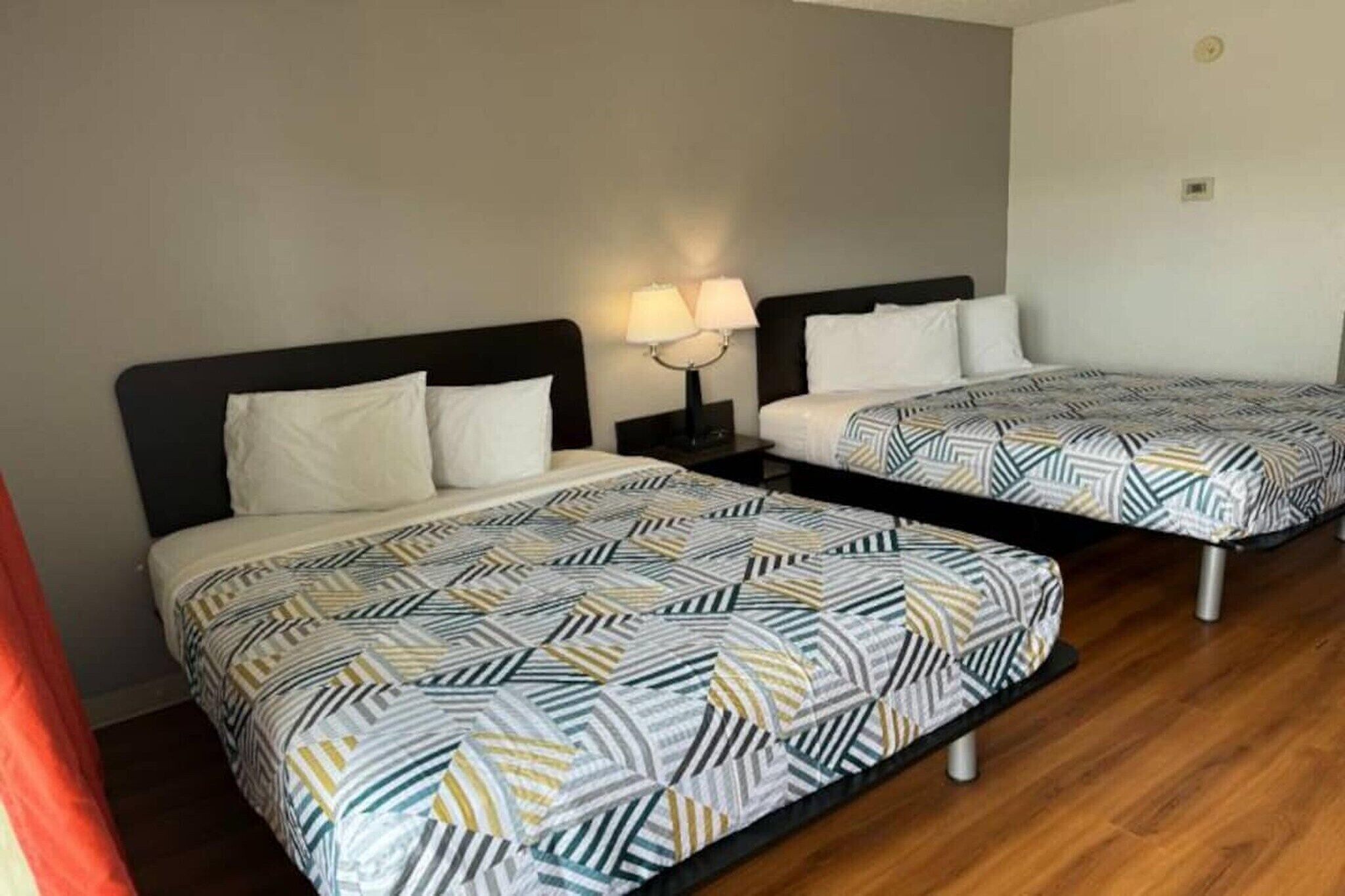 Two single beds with patterned bedding, a nightstand with a lamp, and a wooden floor.