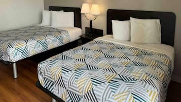 Een hotelkamer met twee eenpersoonsbedden, elk voorzien van een bedovertrek met patroon en witte kussens. Er staat een nachtkastje met een lamp tussen de bedden.