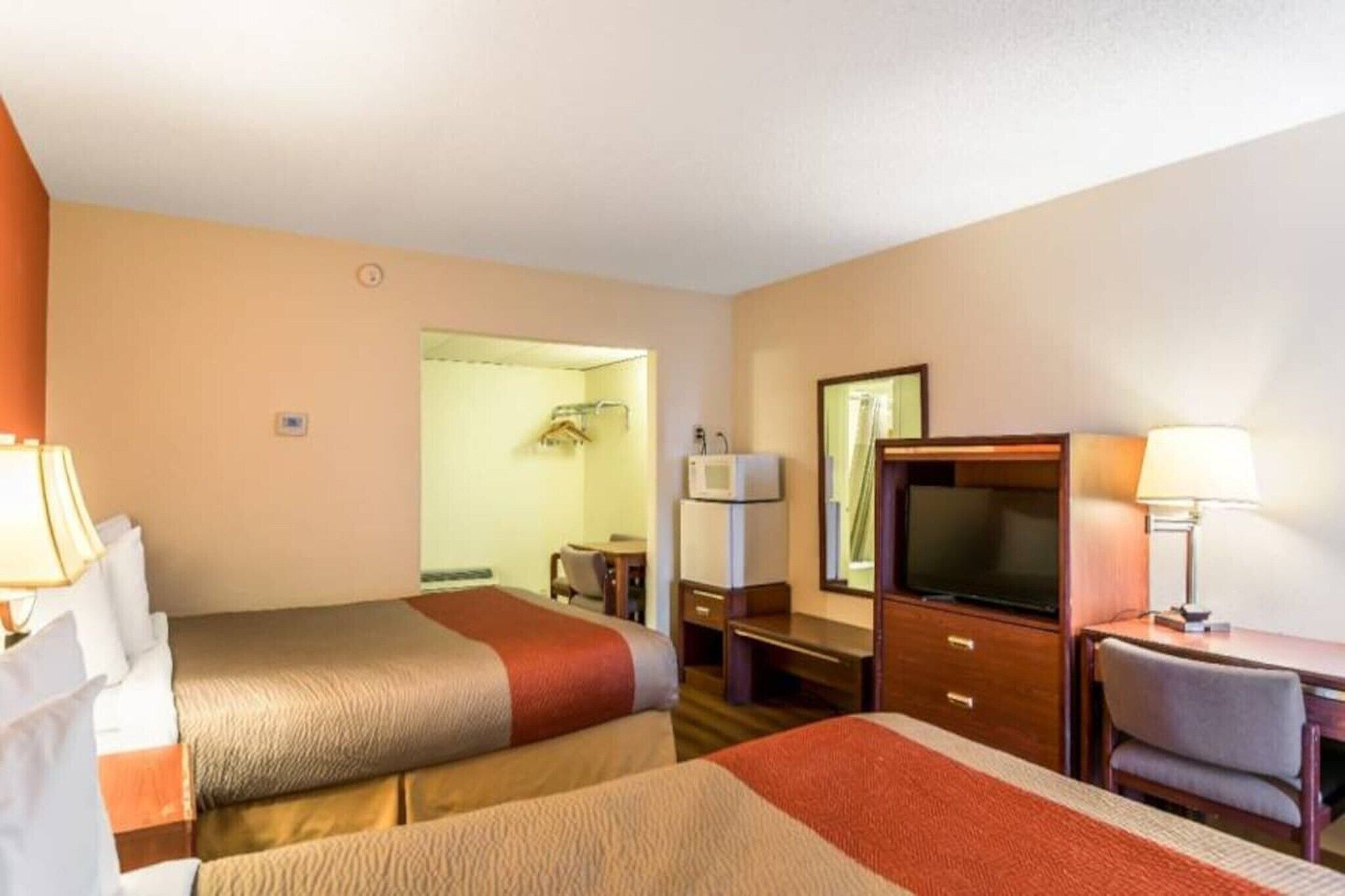 A hotel room with two beds, a desk, a television, and a mirror.