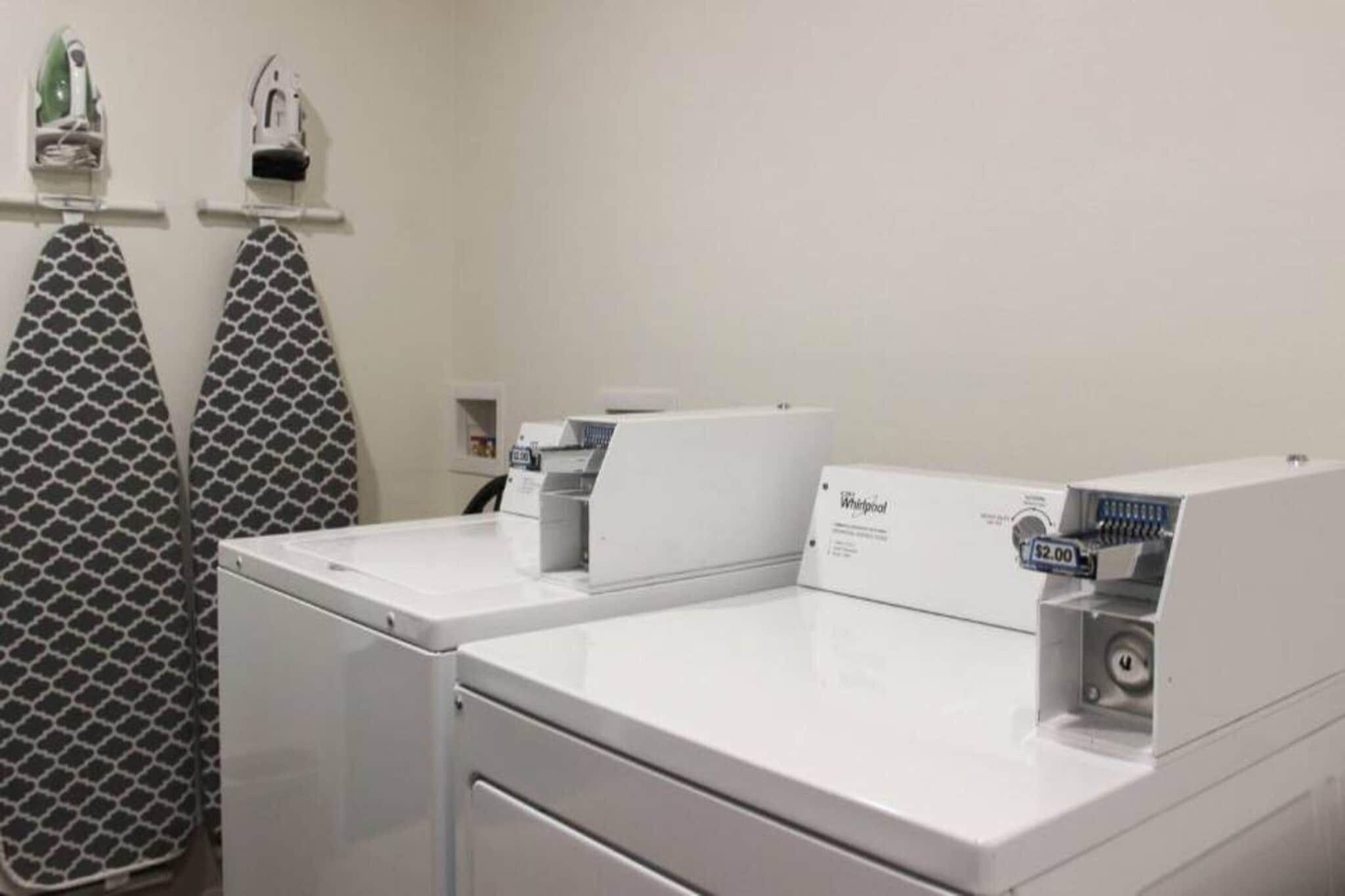Un espace buanderie équipé de deux lave-linge Whirlpool, d’un porte-serviettes à motifs et d’une petite étagère contenant divers objets.