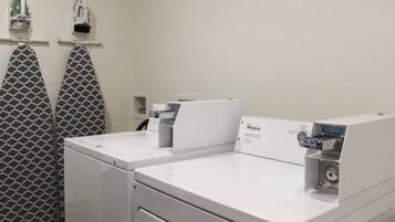 Un espace buanderie équipé de deux lave-linge Whirlpool, d’un porte-serviettes à motifs et d’une petite étagère contenant divers objets.