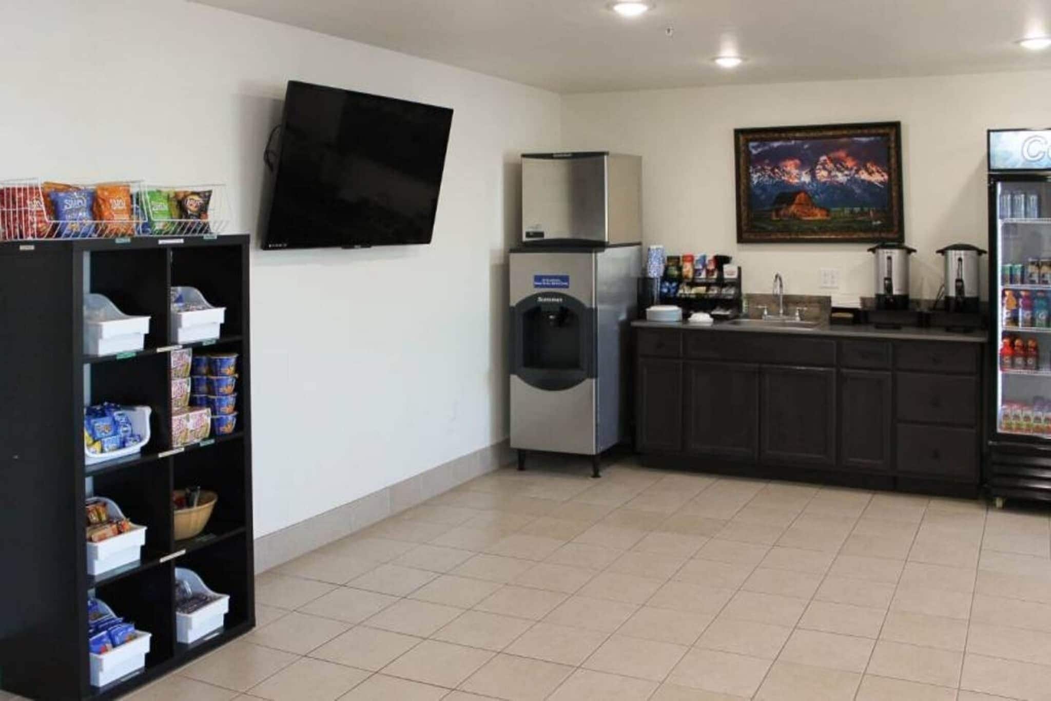 Une pièce propre et bien éclairée, avec un téléviseur à écran plat fixé au mur, un réfrigérateur, un distributeur d’eau et une machine à café posée sur le comptoir.