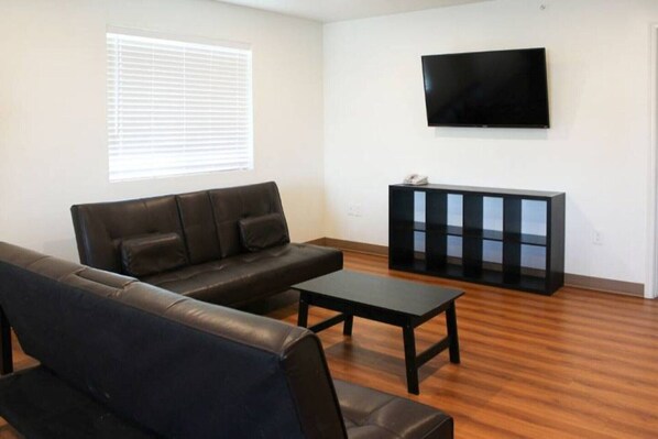 A living room with a sofa, a coffee table, a TV, and a cabinet. - Cozy 2 Queen Beds|Vending Machine (Rexburg)