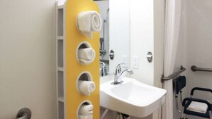 Ein Badezimmer mit einem weißen Waschbecken, einem Spiegel und einem gelben Handtuchhalter mit vier Handtüchern.