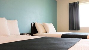 Habitación de hotel con dos camas, una mesita de noche y un ventanal con cortinas.