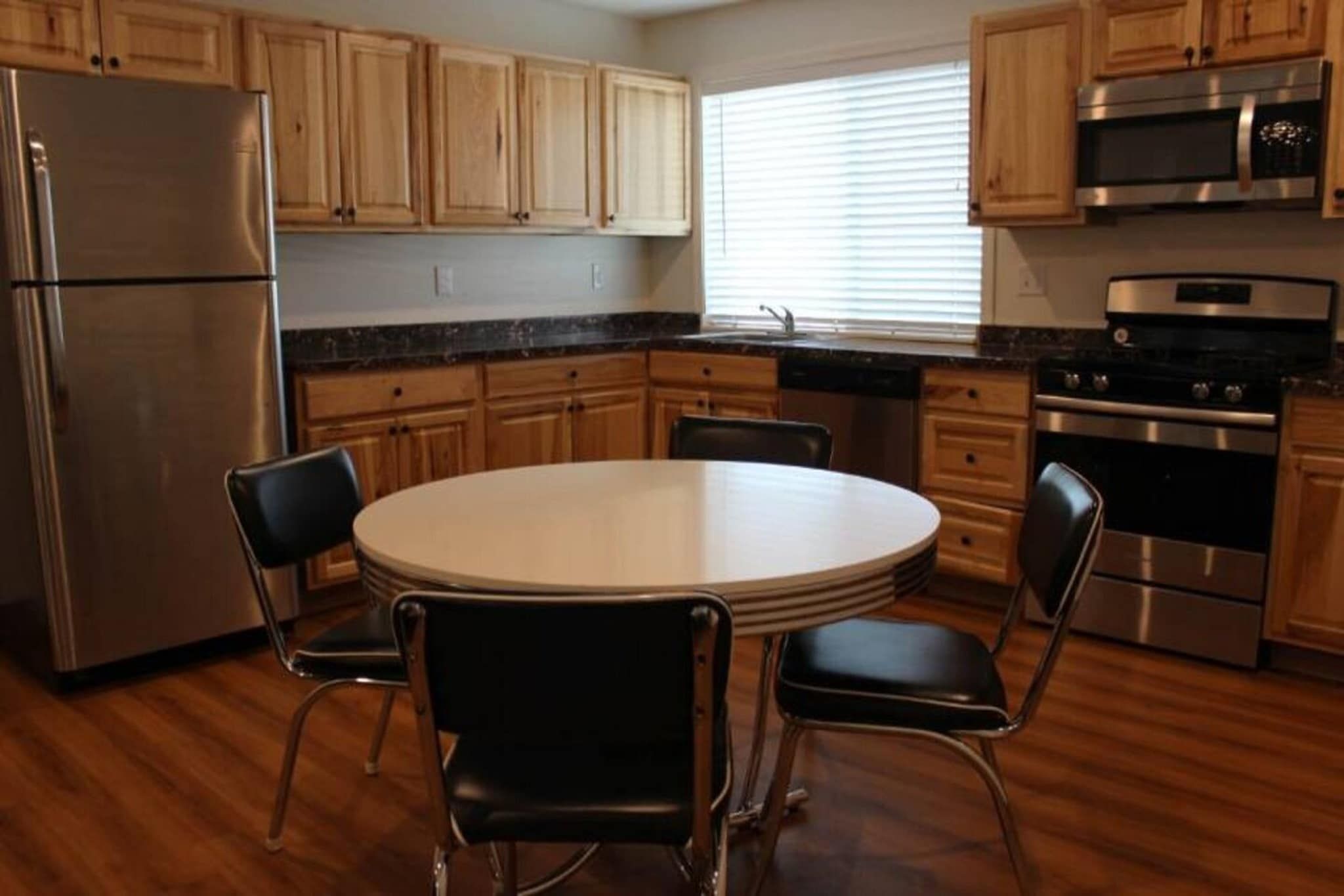 Une cuisine avec des meubles de rangement en bois, un réfrigérateur en acier inoxydable, une cuisinière et une table à manger avec des chaises.