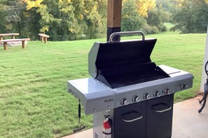 A portable gas grill with four burners and a side burner, placed on a concrete patio.