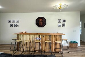 Eine Bar mit einem Holzboden, einer Holztresen und Barhocker, einem Schild mit der Aufschrift 'GOAL HOUSE' und gerahmten Bildern an der Wand.