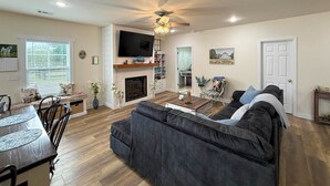 A living room with a fireplace, a sofa, a dining table with chairs, and a television mounted on the wall. - Hot Tub, Goats, 10 Mins to Sheriff's Jeep Fest! (Dawsonville)