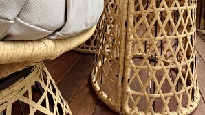 A wicker chair with a cushion and a woven stool against a wooden wall. - Refuxio da Carballeira - Cabin 1 (pet-friendly) (Rebordelo (San Martiño))