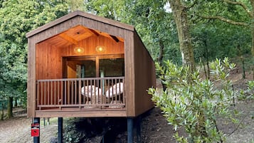 Une cabane en bois dotée d’un balcon, entourée d’arbres.